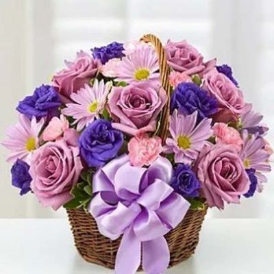 Hand-designed in a charming handled basket and accented with a satin ribbon, this Basket of Blossoms is sure to make her smile. This beautiful arrangement is filled with roses, lisianthus and daisies in rich shades of purple and lavender.