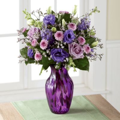 Elegant and chic, this flower bouquet is laced in lavender to send your love, kindness, and gratitude to your recipient this spring season. Lavender roses and purple double lisianthus flaunt their twilight inspired beauty, mingling amongst purple button poms, purple larkspur, pink limonium, and lush greens, presented in a purple swirled glass vase. The perfect thank you, birthday, or Mother's Day gift.